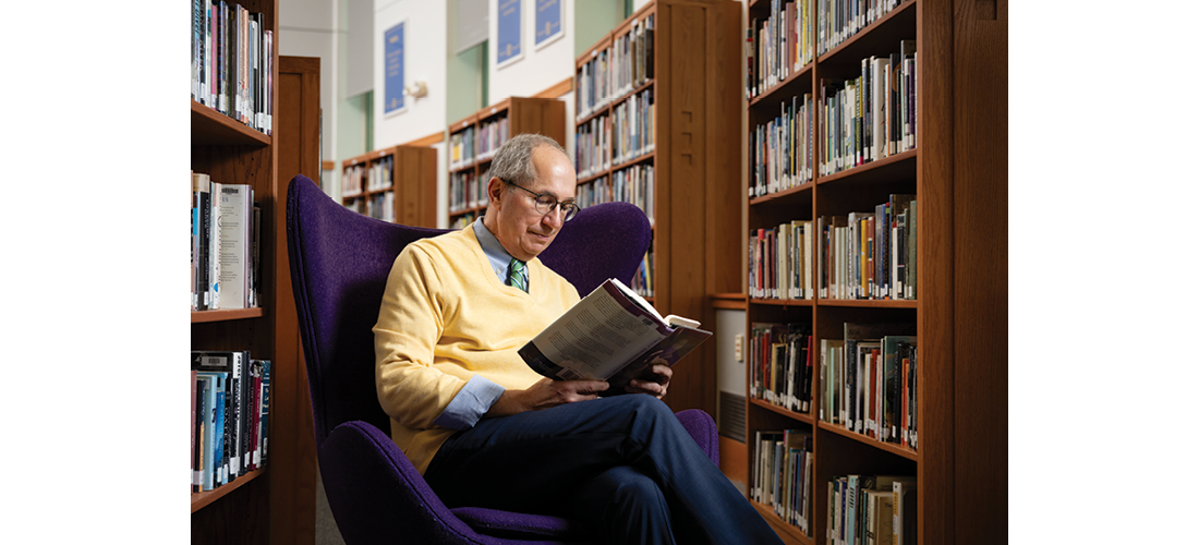 Man in a library sitting in an armchair reading a book