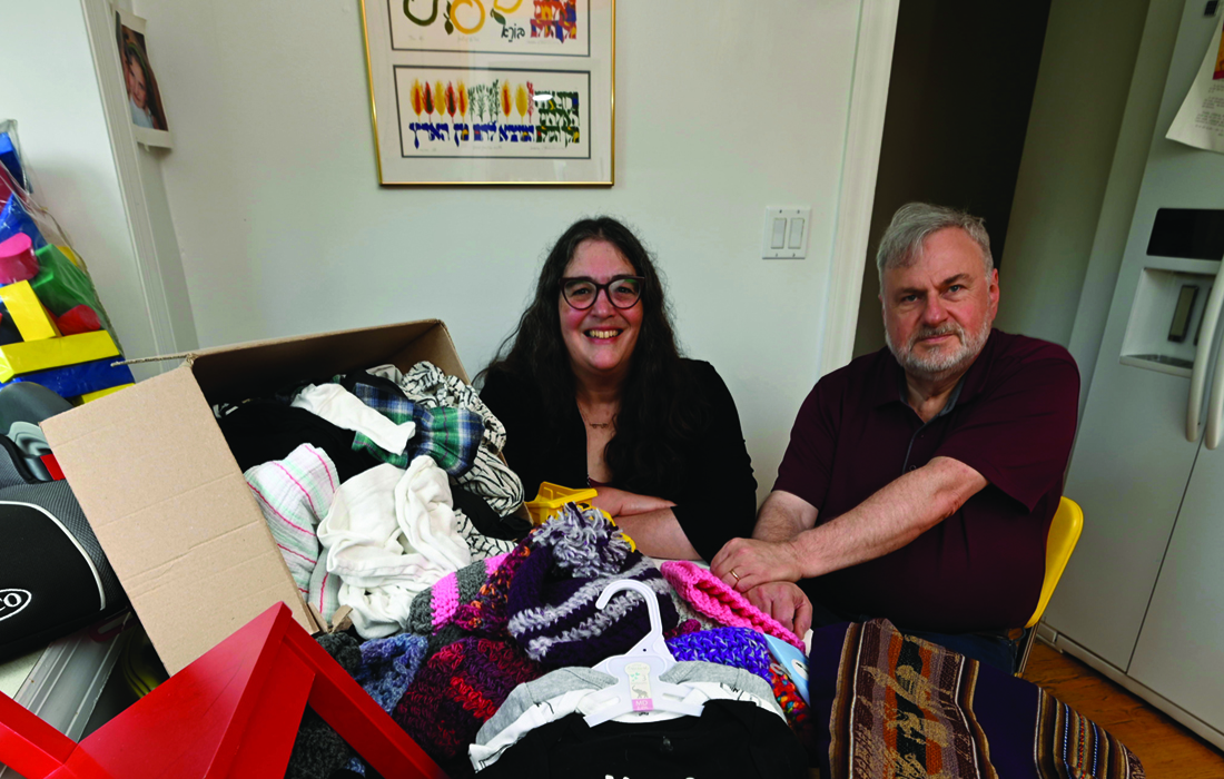 Woman and a man sitting in a dining room behind a table piled with donated clothes and toys