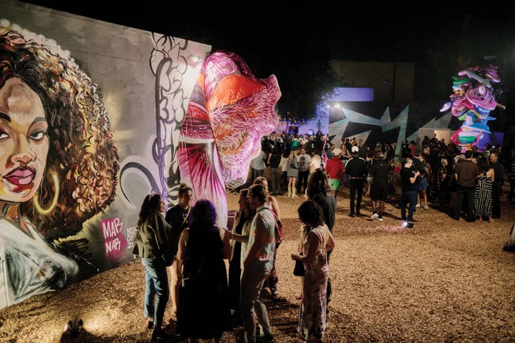 People milling around a mural with a party in the background