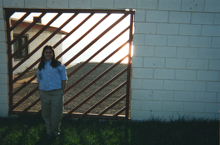 Chelsea as a teen standing in front of a barred gate and high cinderblock wall