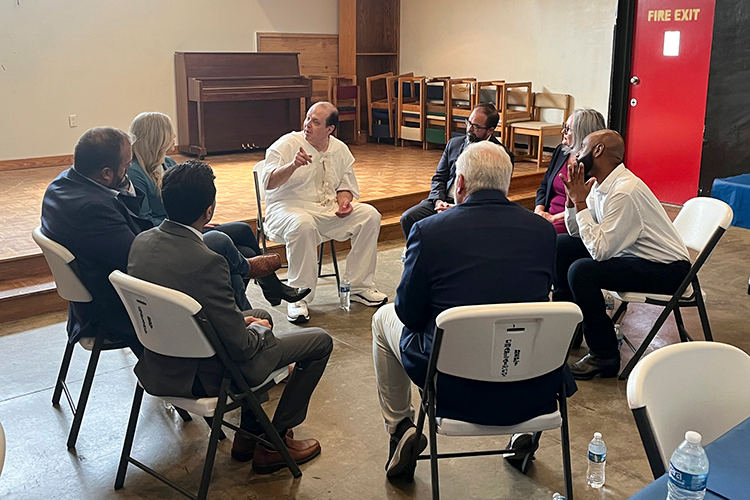 Circle of people seating in chairs, with a man in a white prison uniform speaking