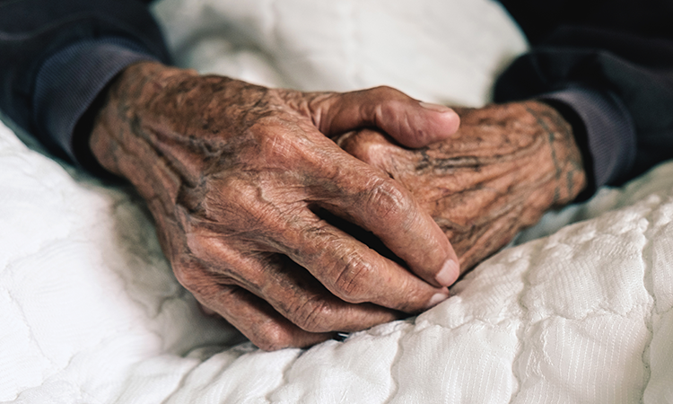 elderly man's hands as he lies in bed