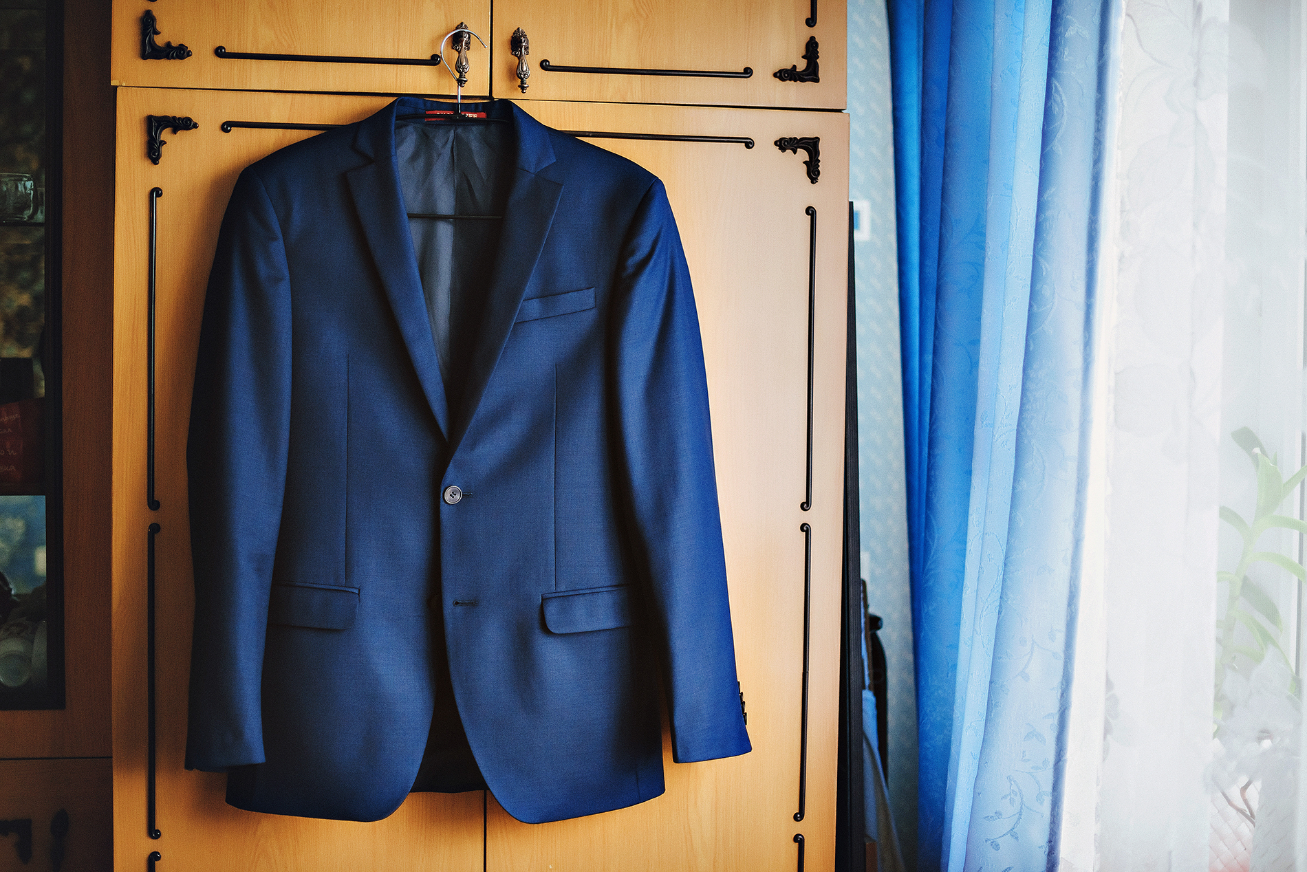 A blue suit jacket hanging on a dresser next to a curtained window